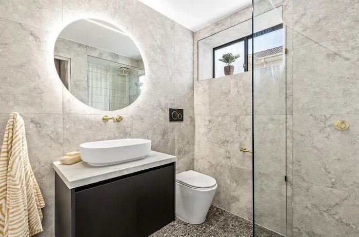 Elegant bathroom with a round backlit mirror, dark vanity and gold tapware