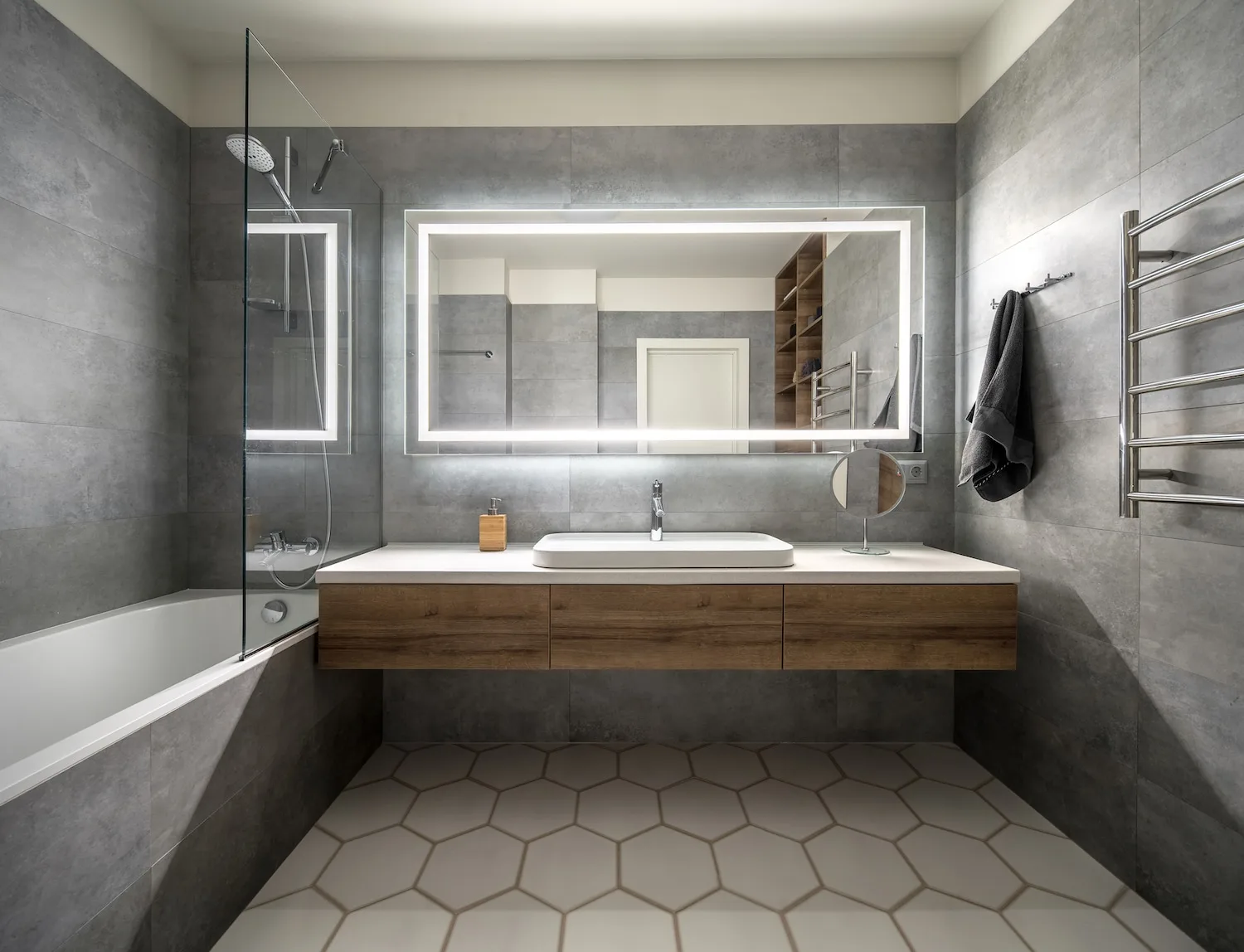Grey stone bathroom with a backlit mirror, gold tapware and a timber vanity