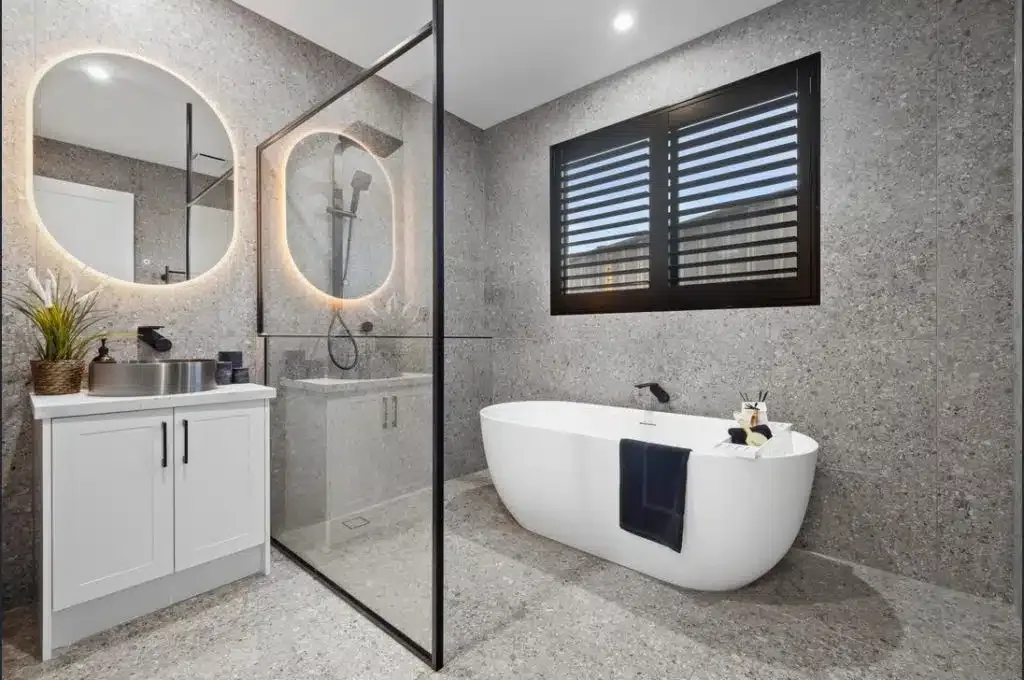 Terrazzo-tiled bathroom with a round mirror and freestanding tub